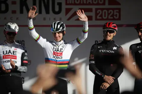 Ciclista in maglia iridata con le mani alzate sul palco, tra ciclisti UAE e Tudor, davanti al fondale BEKING Monaco
