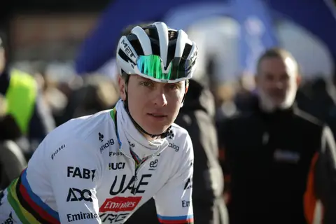 Primo piano di ciclista in maglia iridata UAE, casco bianco e occhiali a specchio verdi, con la folla sfocata dietro