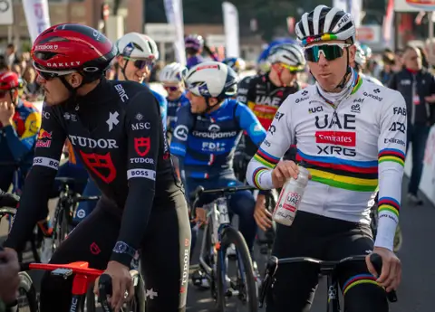 Ciclisti fermi in sella: uno in maglia iridata con la borraccia in mano, accanto uno in maglia nera Tudor