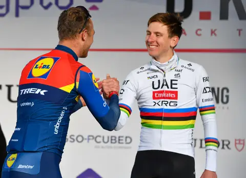 Stretta di mano sul palco tra due ciclisti: uno in maglia Lidl-Trek, di spalle, e uno in maglia iridata che sorride