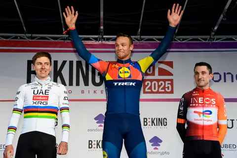 Tre ciclisti sul palco davanti al fondale BEKING Monaco; chi sta al centro, in maglia Lidl-Trek, alza le braccia