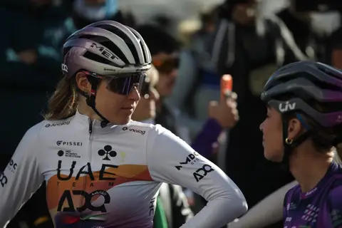 Primo piano di ciclista in maglia UAE Team ADQ e casco MET; a destra, di profilo, ciclista con casco Liv e maglia viola
