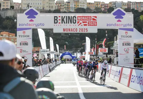L’arco BEKING Monaco sulla strada, con un gruppetto di ciclisti che avanza e gli spettatori in primo piano