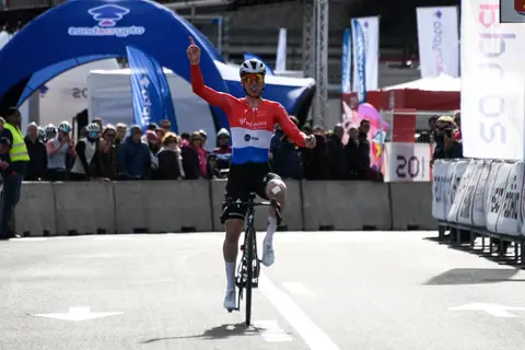 Ciclista in maglia rossa, bianca e blu SD Worx con un braccio alzato e l’indice teso, davanti al pubblico