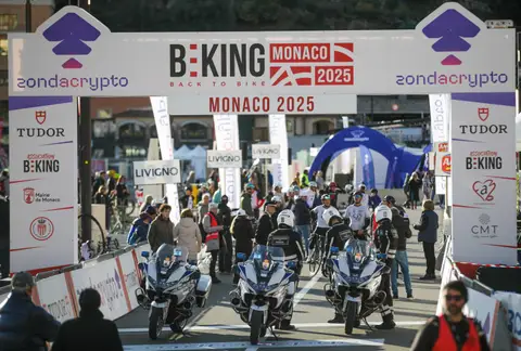 L’arco BEKING Monaco con tre moto e agenti in primo piano; dietro, ciclisti, pubblico e una tenda blu