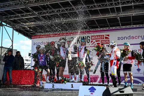 Ciclisti sul podio con champagne spruzzato e mazzi di fiori, davanti al fondale BEKING Monaco