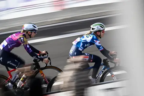 Due ciclisti affiancati ripresi in panning, uno in maglia viola SD Worx e uno in bianco e blu, sfondo mosso