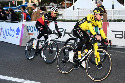 Due ciclisti affiancati lungo le transenne, uno in maglia gialla e nera, l’altro in maglia nera con dettagli rossi