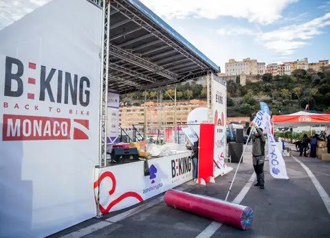 Il palco BEKING Back to Bike Monaco in allestimento: un uomo sistema un’asta con bandiera, a terra un rotolo rosso