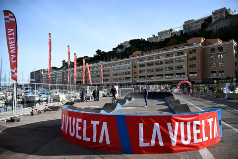Pump track La Vuelta: un ciclista sulla pista, bandiere, il porto e i palazzi dietro