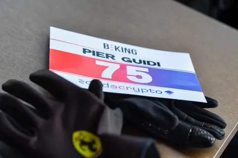 Pettorale BEKING numero 75 appoggiato su un tavolo accanto a guanti neri da ciclismo