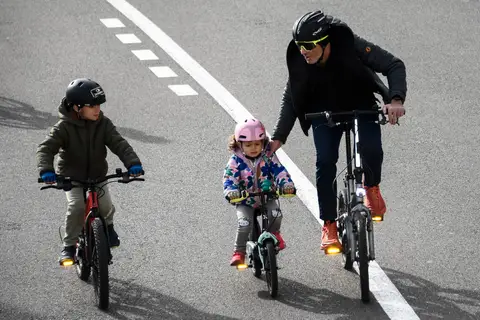 Due bambini e un adulto in bici affiancati; l’adulto tiene una mano sulla spalla del più piccolo, ripresa dall’alto