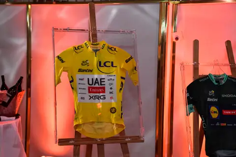Maglia gialla del Tour de France incorniciata su un cavalletto; a destra, parte di una maglia verde scuro Lidl-Trek