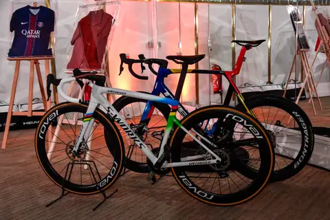 Due biciclette da corsa esposte su moquette davanti a maglie incorniciate su cavalletti, con pareti a luci rosa